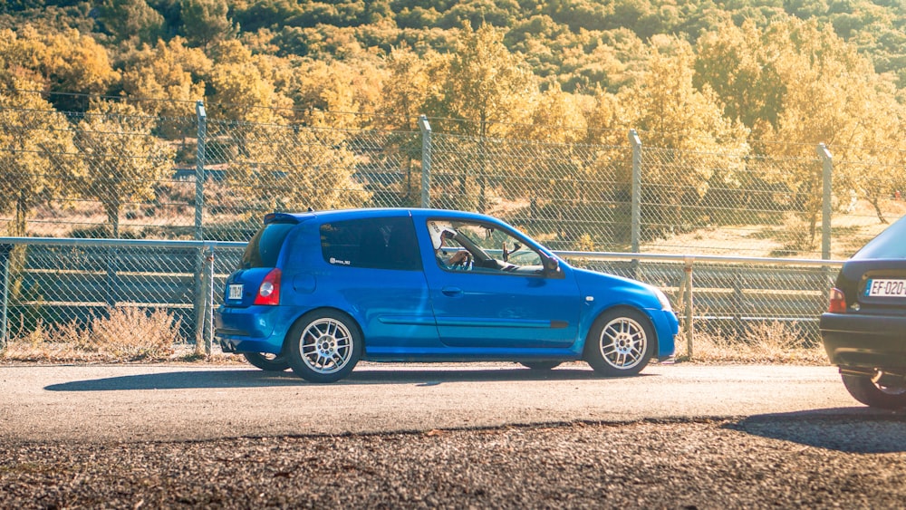 blue 5 door hatchback parked beside gray metal fence during daytime