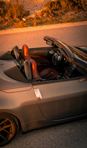 Sporty convertible with the top down on an open road, shining under a sunset sky.