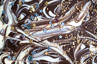 Swirls of milk and dark chocolate are decorated with small golden and silver star-shaped sprinkles, along with scattered bits of crushed nuts.