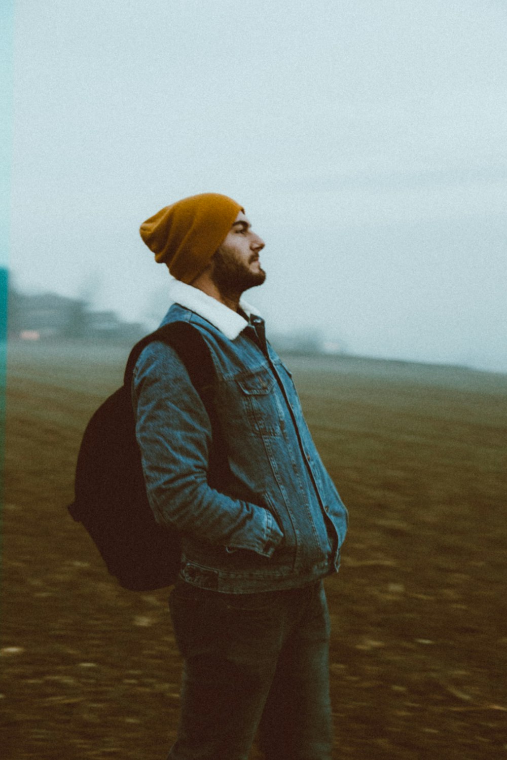 man in blue denim jacket and brown knit cap standing on brown field during daytime