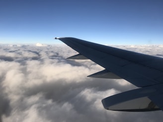 A sleek airplane wing cutting through clear blue skies above fluffy white clouds.