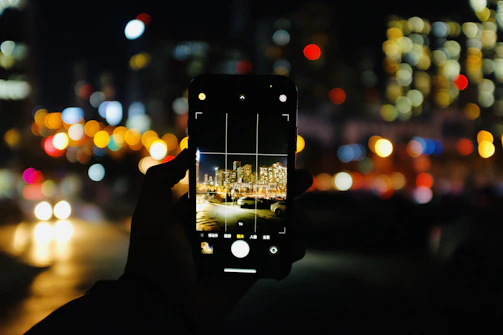 Close-up of a smartphone camera lens reflecting vibrant city lights at night.