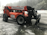 Large orange forklift-style construction vehicle with 'EquipmentShare' branding, parked on a wet and slightly snowy surface, surrounded by a misty forest and power lines in the background.