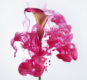 A flower with a pink and brown bloom sits in the center, surrounded by vibrant pink ink swirls that give the appearance of smoke or flowing fabric. The background is a pale, almost white tone, emphasizing the vividness and fluidity of the pink ink.