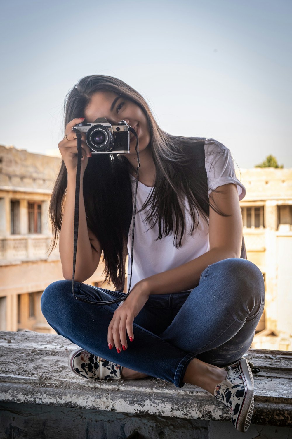 mulher na camiseta branca e jeans azul sentada no banco de concreto segurando a câmera durante