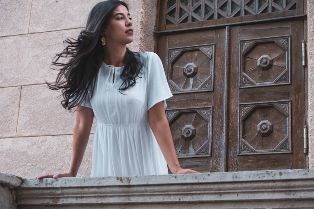 woman in white dress standing near brown wooden door