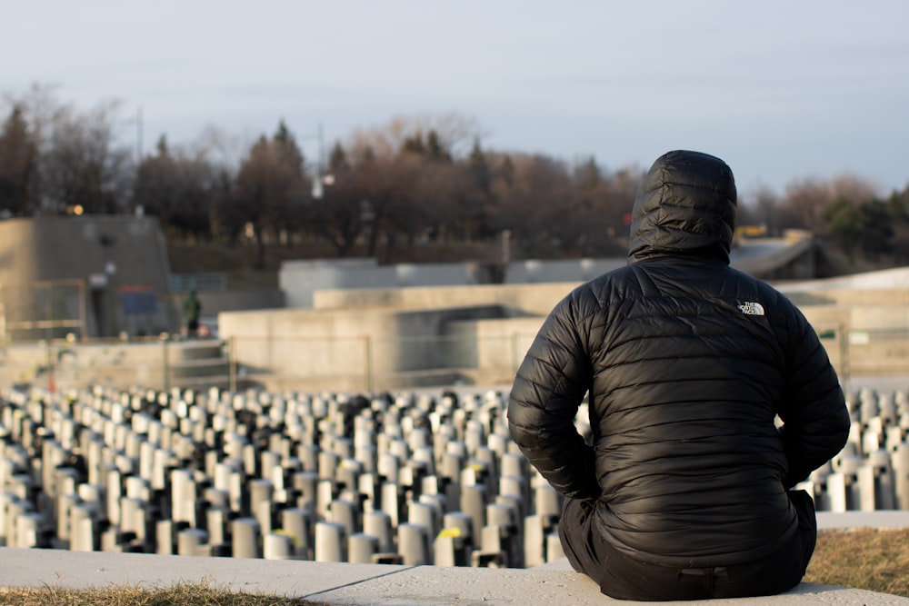 man in black jacket and brown pants sitting on gray concrete bench during daytime