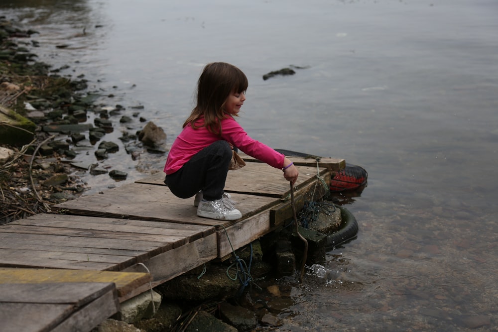 girl in purple jacket and blue denim jeans holding brown wooden boat on body of water