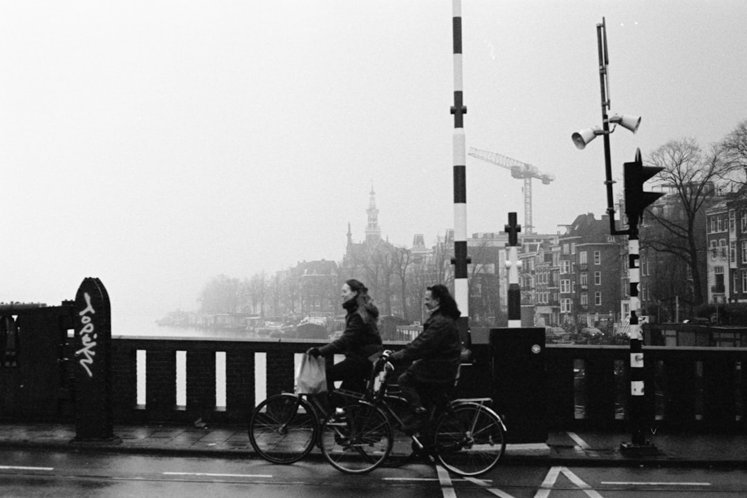 grayscale photo of man and woman sitting on bench near city buildings