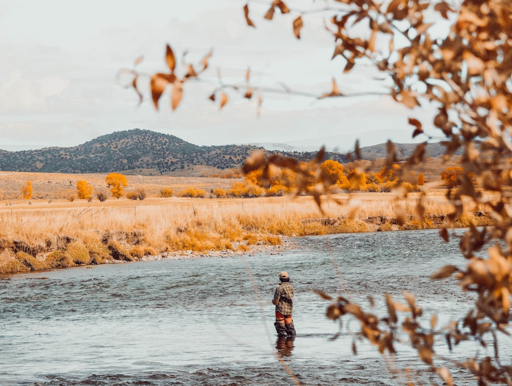 a man standing in a river next to a dry grass field