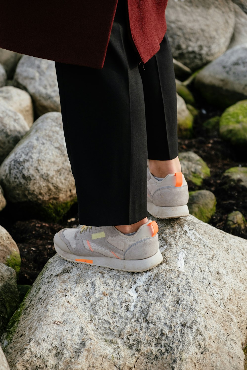 person in black pants and white sneakers standing on gray rock