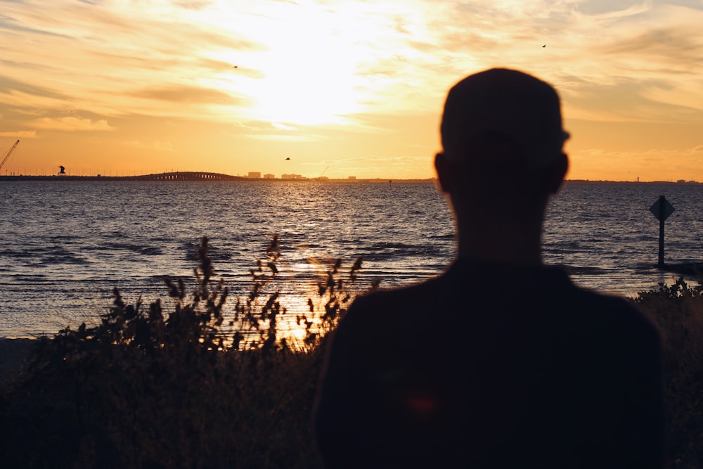 homme en chemise à col rond noir debout sur le champ d’herbe verte au coucher du soleil