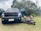 A large black Ford pickup truck with its front doors open is parked on grass. In front of the truck are two small quad bikes, one blue and one pink with helmets placed on their seats. The background consists of trees and cloudy sky.