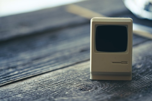 A miniature vintage computer model on a wooden surface, focused on the intricate details of the retro design with a blurred background.