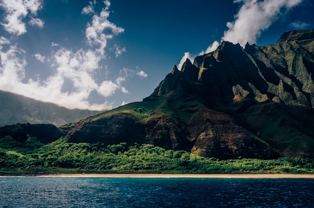 green and brown mountain beside blue sea under blue sky and white clouds during daytime