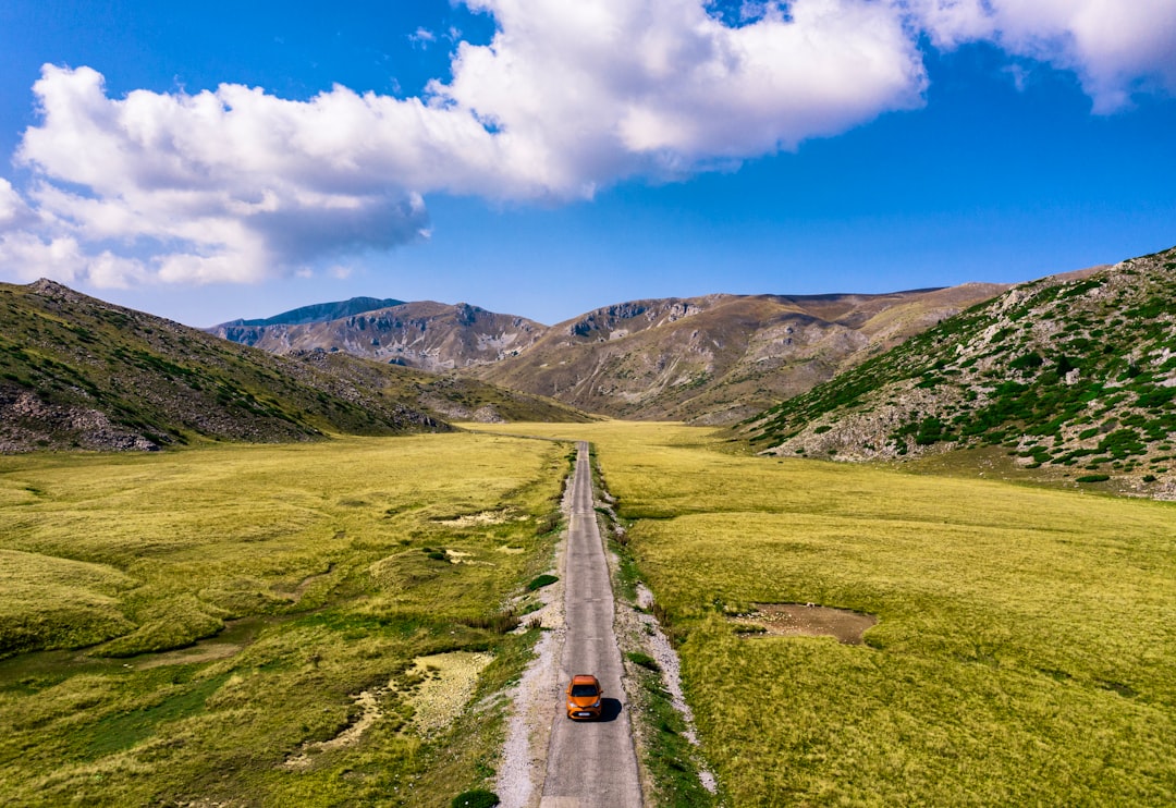 gray concrete road between green grass field under blue sky during daytime