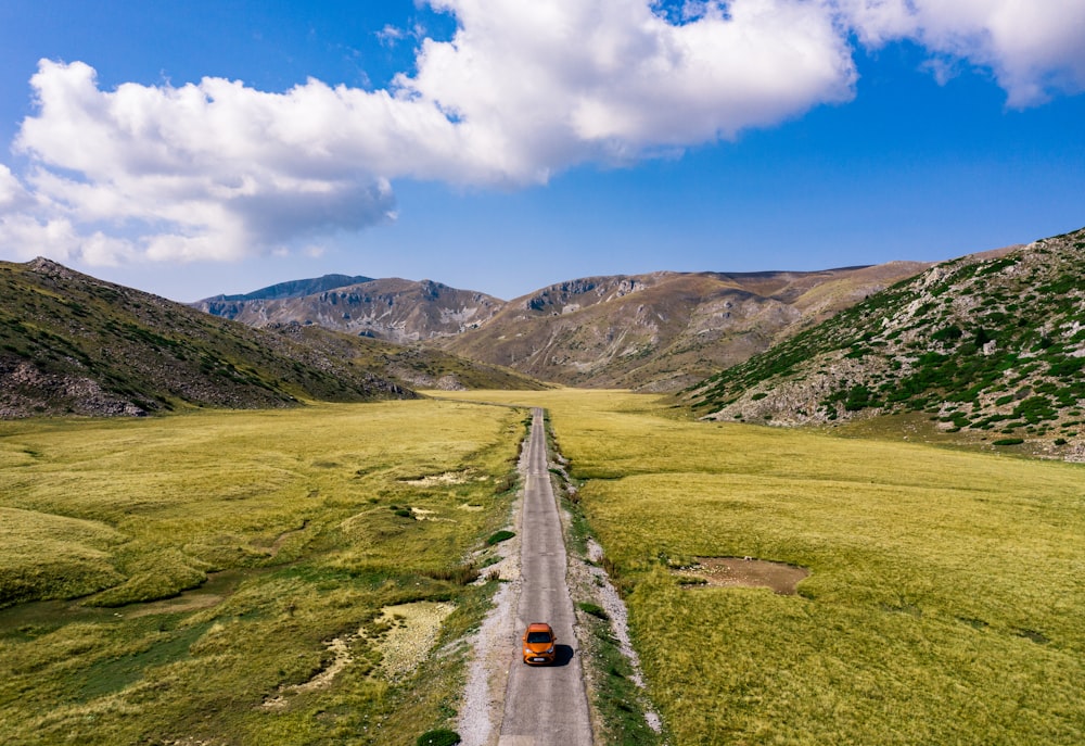 gray concrete road between green grass field under blue sky during daytime