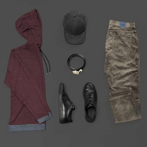 Overhead shot of a minimalist outfit laid out on a slate grey background featuring tees and accessories