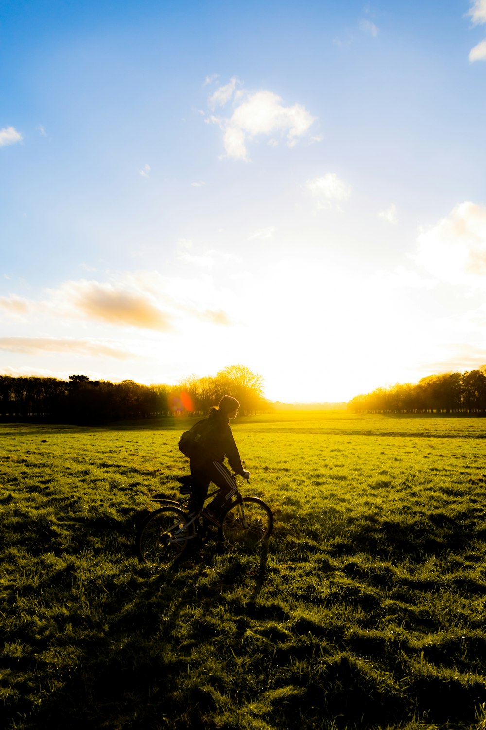 man riding bicycle on green grass field during sunset