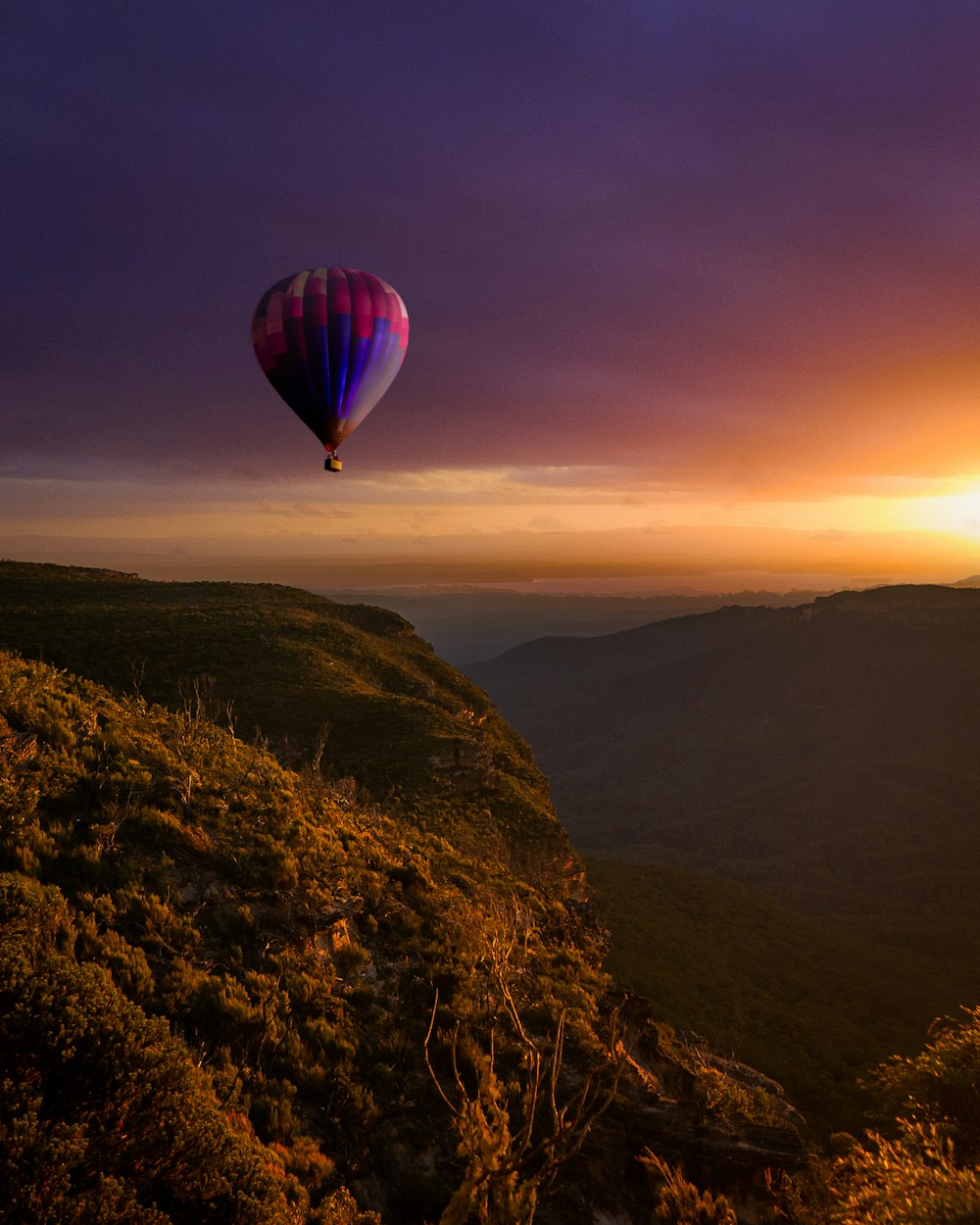 Heißluftballon fliegt bei Sonnenuntergang über die Berge