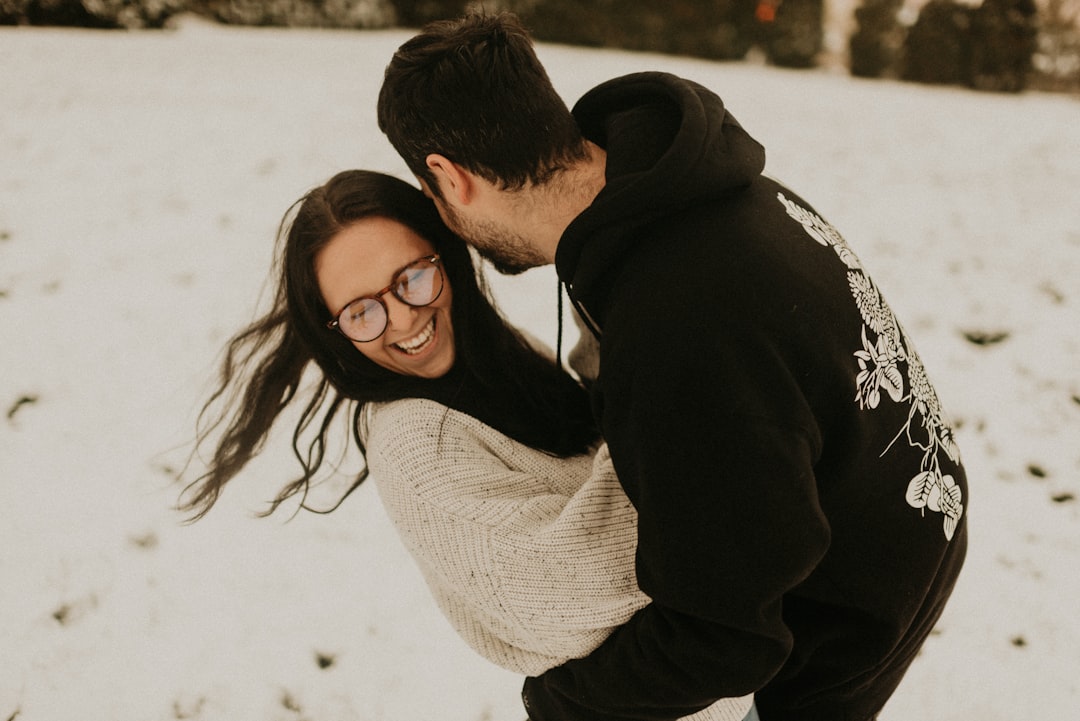man in black hoodie kissing woman in white knit sweater