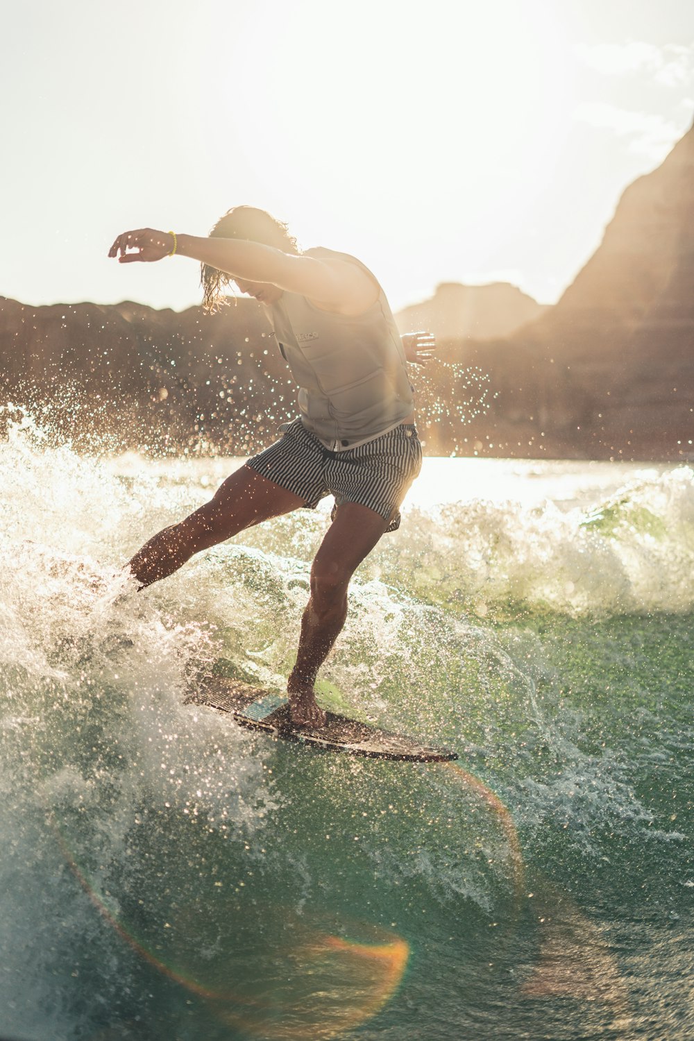 Mann in weißem Tanktop und blauen Shorts beim Surfen auf Meereswellen tagsüber