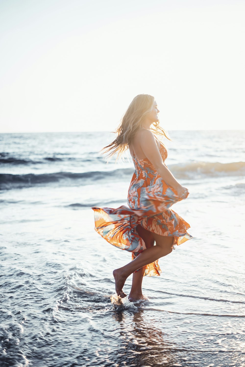 Frau in orangefarbenem Kleid, die tagsüber am Strand spazieren geht