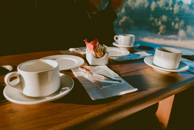 A bright, sunlit table set with cheerful ceramic plates and cups ready for a slow morning.