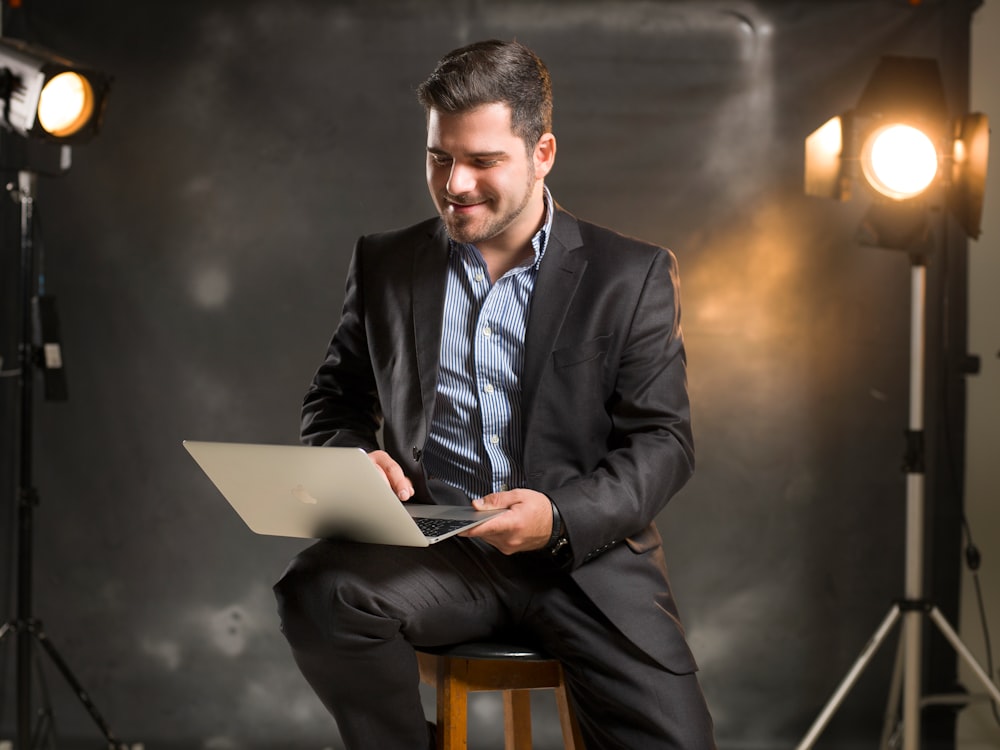 man in black suit jacket sitting on chair using macbook