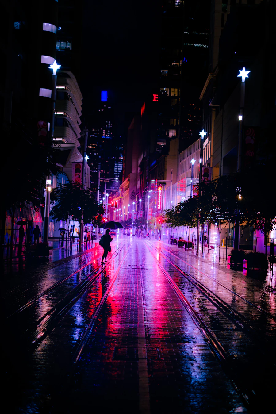 A street washed pink by neon, a lone walker under an umbrella