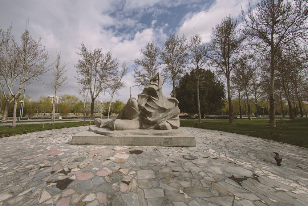 gray concrete statue on green grass field under white clouds and blue sky during daytime