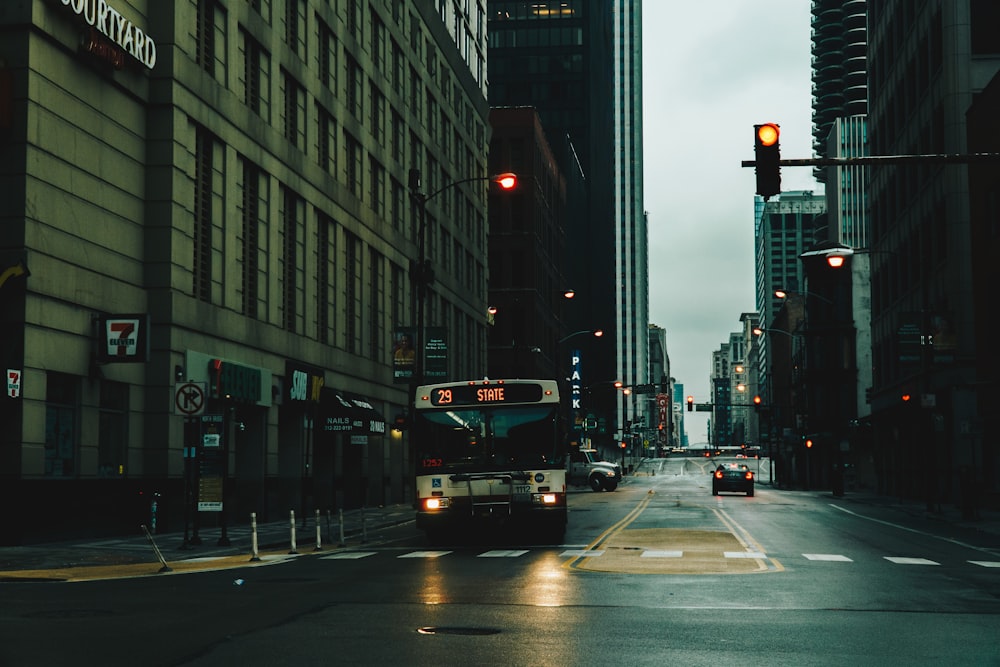 red bus on road in between high rise buildings during night time