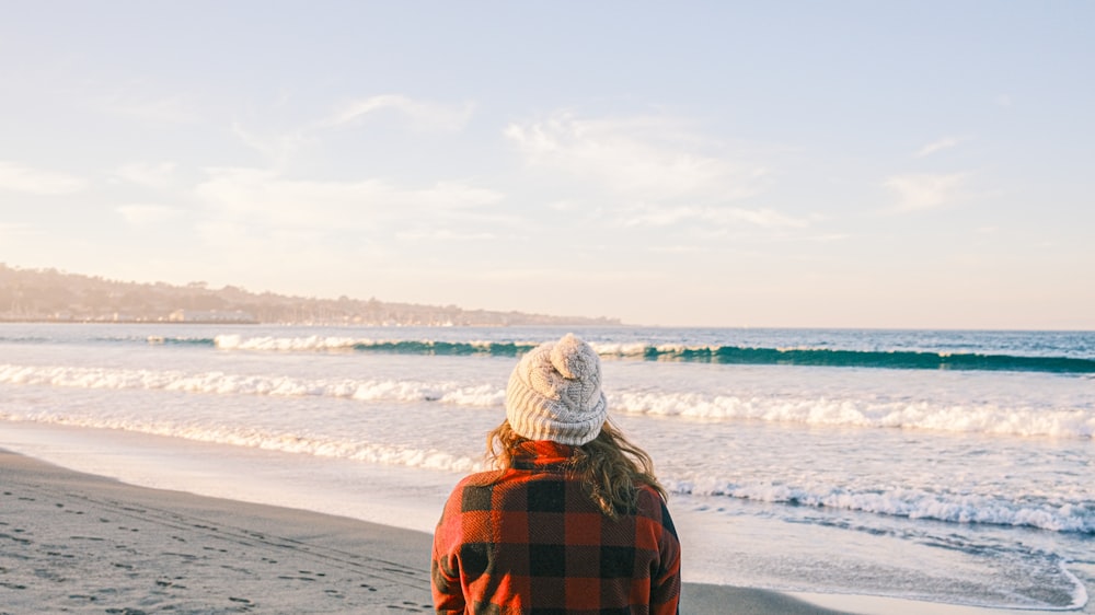 person in orange and black plaid hoodie standing on beach during daytime