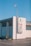 A large billboard on the side of a building displays a Coca-Cola advertisement with the phrase 'Coke adds life to... Nashville.' The building is constructed with white bricks and has an industrial appearance. A windsock in orange is mounted on a pole above the billboard, and the sky is clear and blue.
