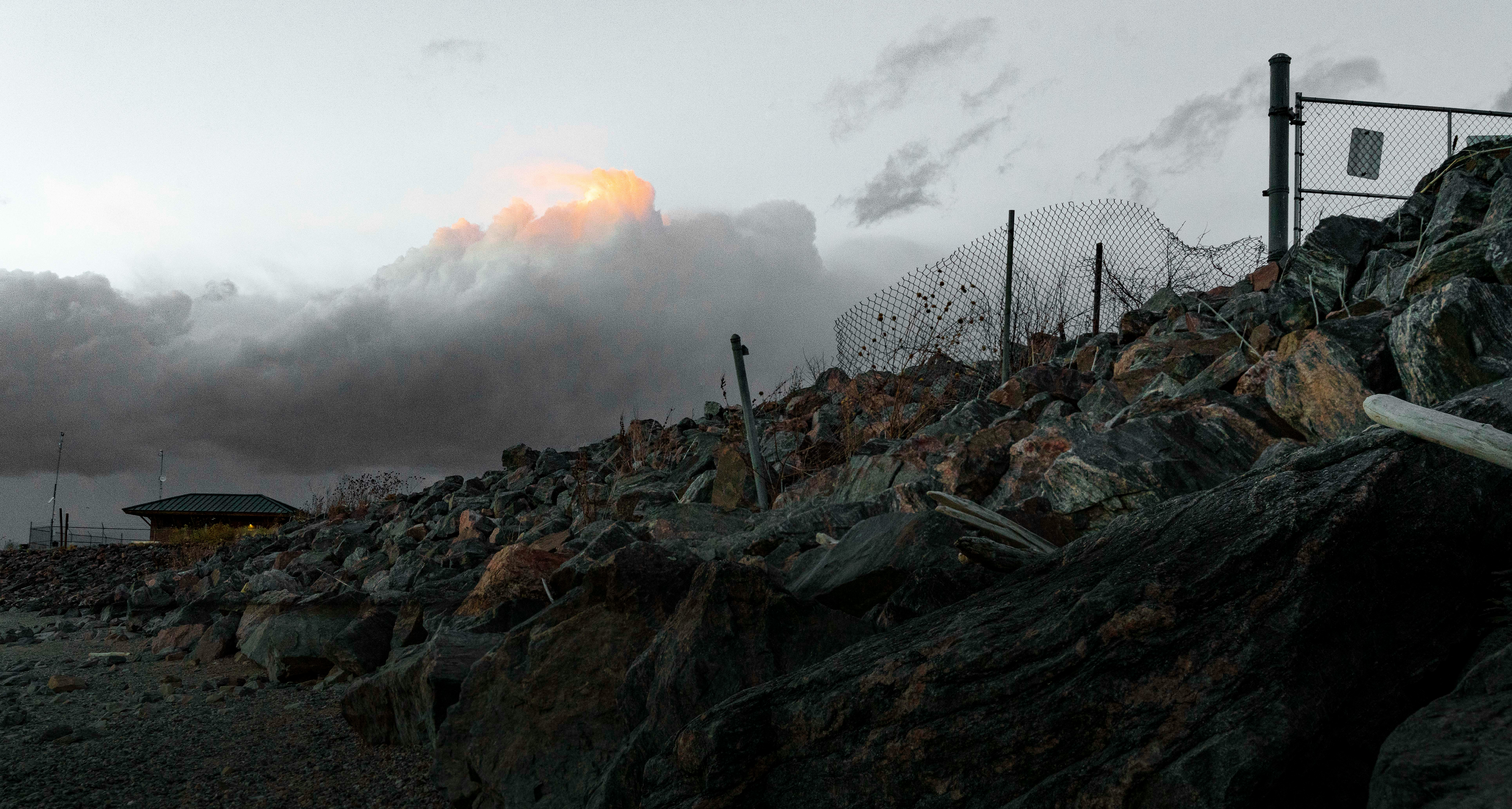 brown rocks near gray metal fence under white clouds during daytime