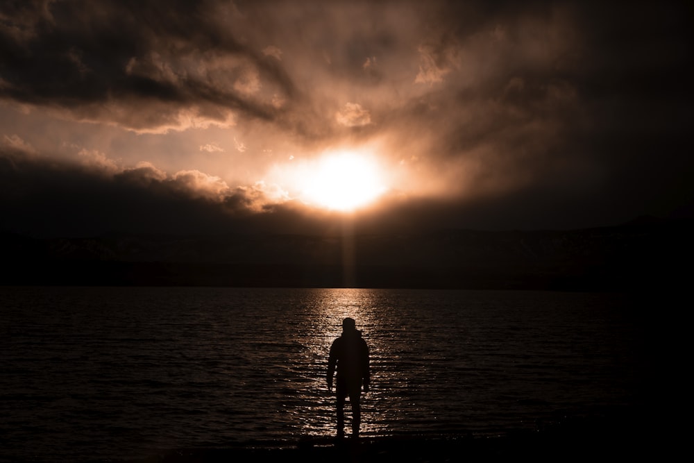 silhouette of 2 person standing on sea shore during sunset