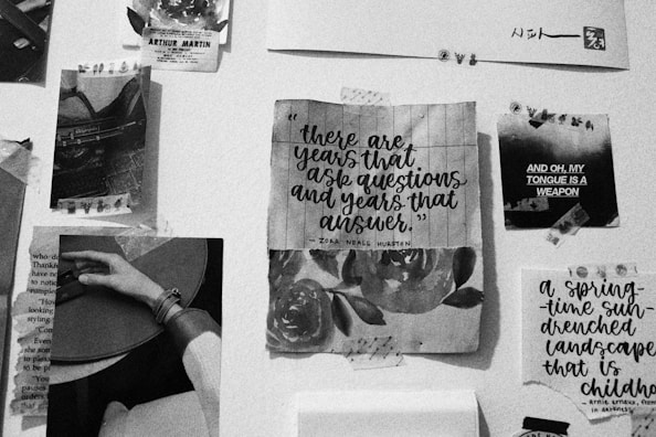 A collage of black-and-white photographs, text, and artwork pinned to a wall. The centerpiece features a quote by Zora Neale Hurston overlaid on a floral background. Nearby are various clippings, including images of a person holding a guitar and abstract text art with phrases like 'AND OH, MY TONGUE IS A WEAPON.'