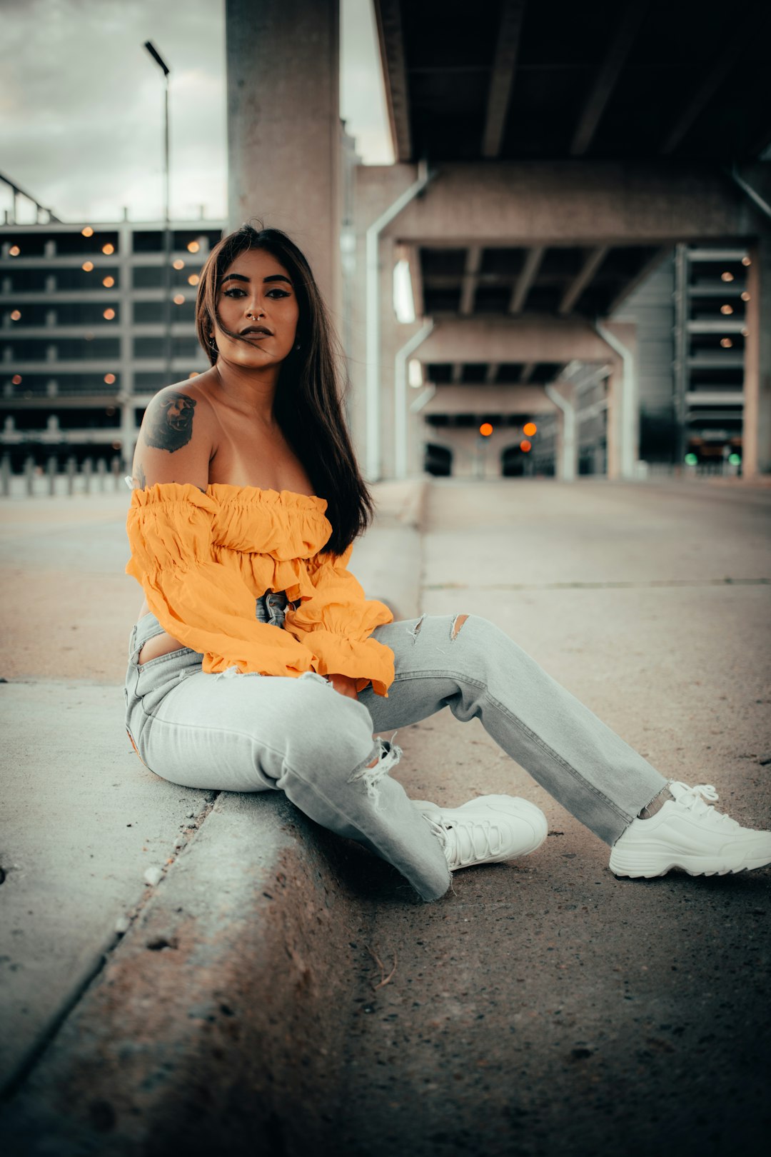 woman in orange off shoulder shirt and white pants sitting on sidewalk during daytime