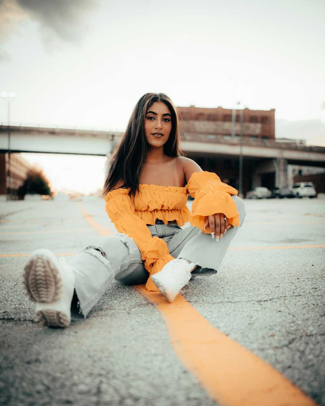 woman in yellow long sleeve shirt and white pants sitting on gray concrete floor during daytime