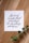 A piece of paper with elegant black calligraphy on a wooden surface, accompanied by a sprig of green eucalyptus.