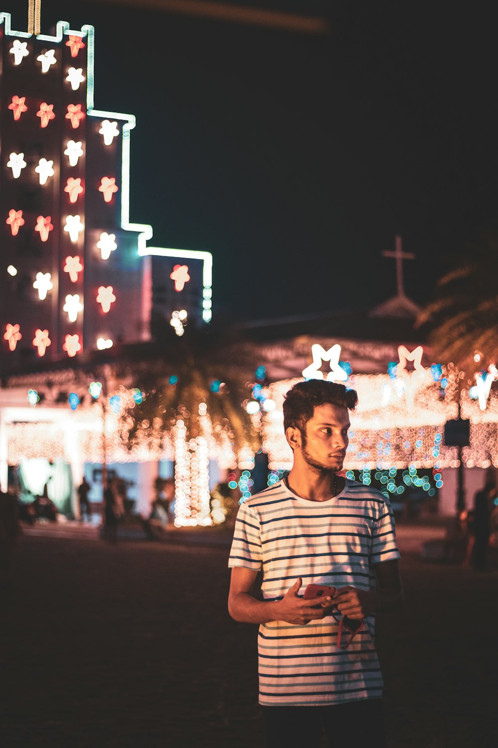 homem em branco e preto listrado camisa do pescoço da tripulação em pé perto do edifício iluminado durante a noite