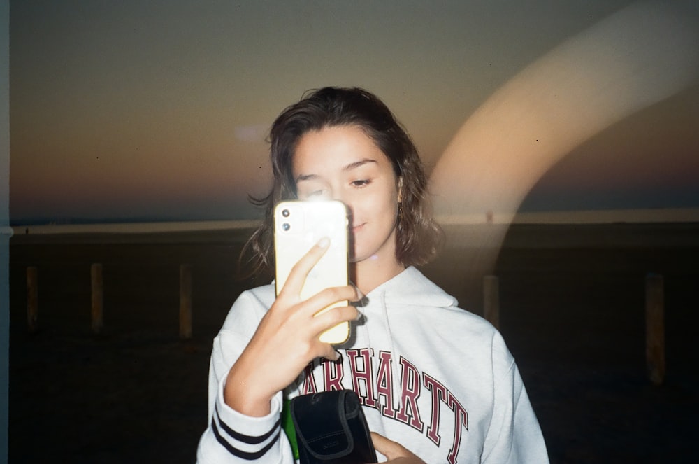 woman in white and black hoodie holding white smartphone