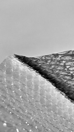 A textured surface of plastic bubble wrap is partially covered by a dark shadow, creating a striking contrast. The bubbles are evenly distributed, and the shadow adds depth and dimension.