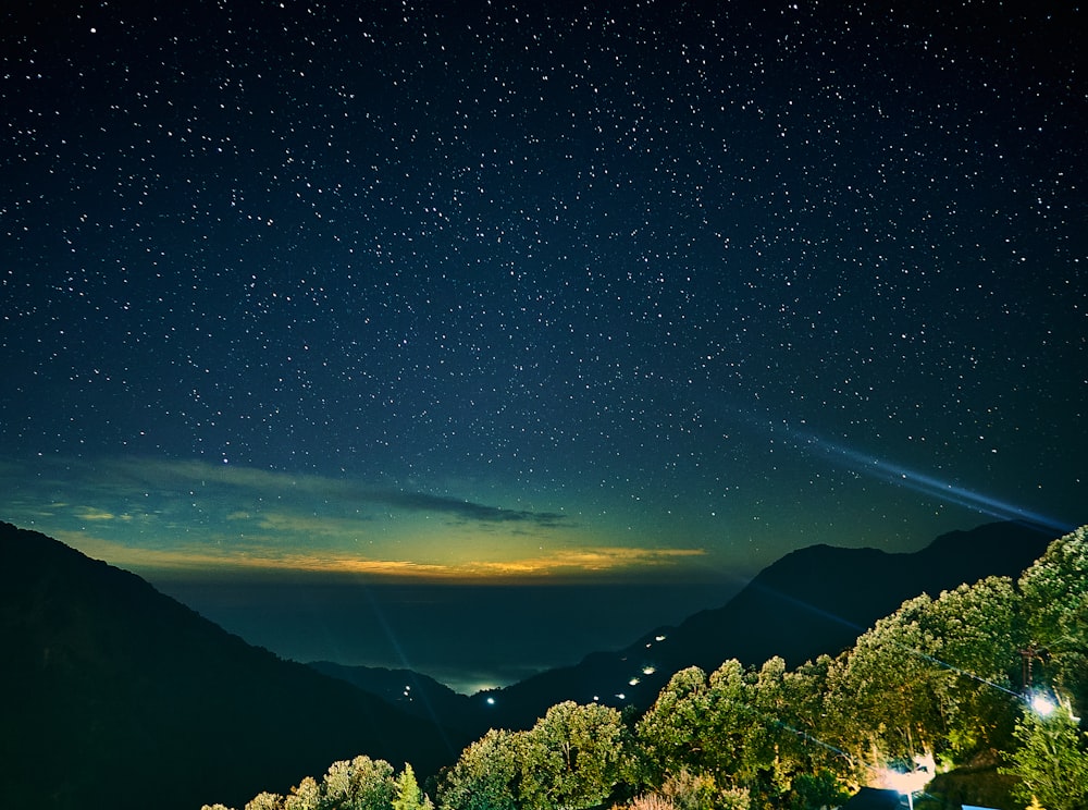 green trees and mountains under blue sky during night time