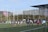 A group of rugby players are engaged in a line-out on a field. Some players are lifting a teammate to catch the ball. The scene takes place in an urban sports facility, with buildings visible in the background.