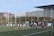 A group of rugby players are engaged in a line-out on a field. Some players are lifting a teammate to catch the ball. The scene takes place in an urban sports facility, with buildings visible in the background.