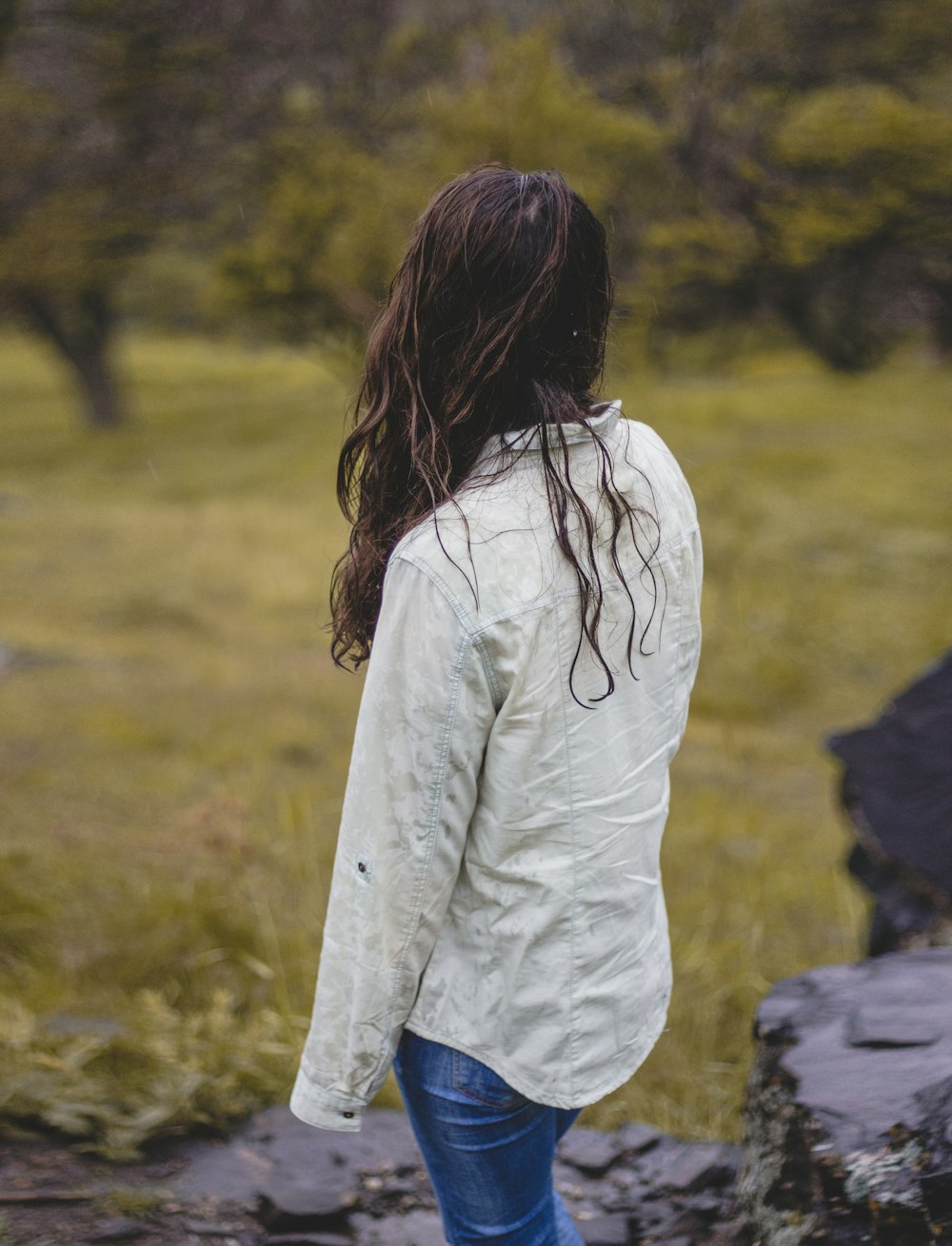 mujer en camisa blanca de manga larga y jeans de mezclilla azul de pie en el campo de hierba verde durante