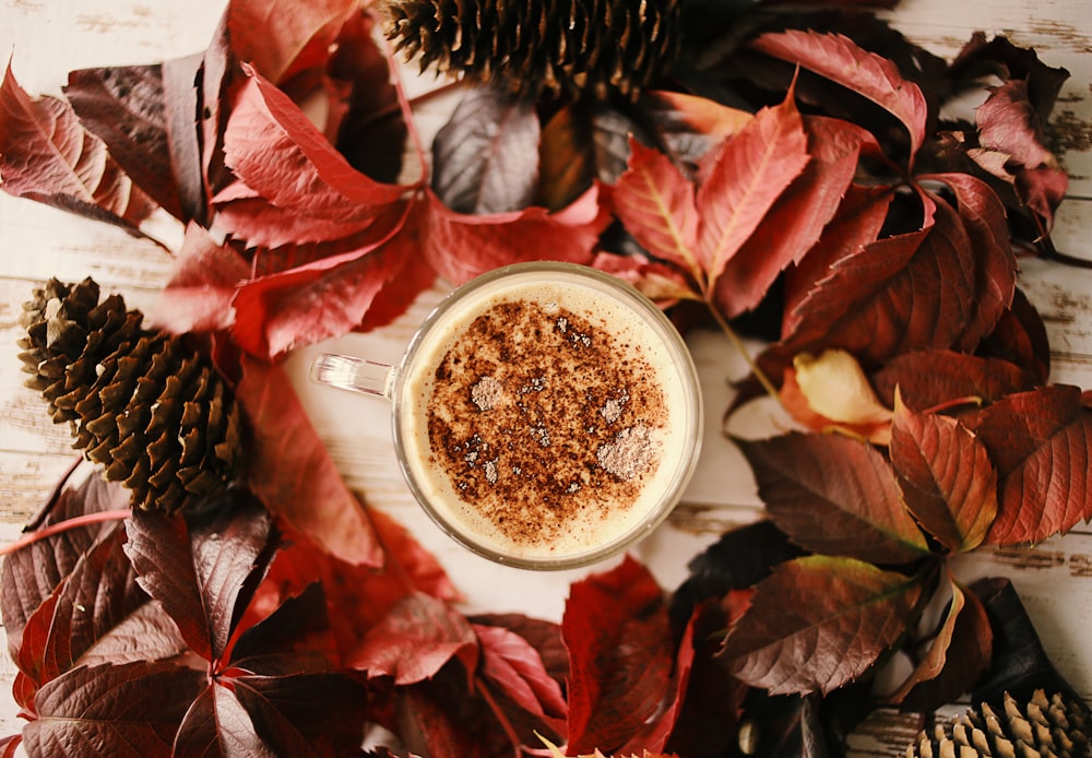 Tasse en céramique blanche avec du café sur des feuilles rouges