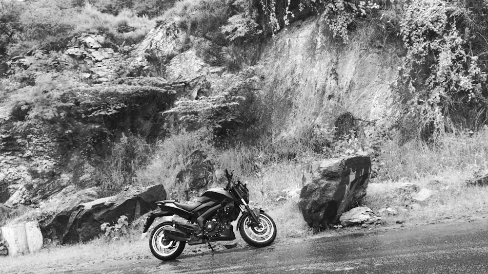 grayscale photo of motorcycle parked beside rock formation