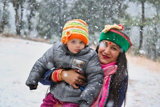 A child and parent bundled in matching knit scarves, laughing in a snowy park.
